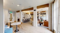 Located at 5026 Zion Rd in Garland, TX, the Atwater Golf Club clubhouse is a thoughtfully designed single-floor amenity space that seamlessly blends rustic warmth with modern sophistication. Throughout the interior, exposed wood ceiling beams contrast beautifully against white shiplap ceilings and whitewashed brick columns, creating a cohesive architectural character that flows from room to room.

The main social area features a striking dark zellige tile fireplace column with a mounted TV, flanked by comfortable lounge seating and woven pendant light fixtures. This gathering space opens into a central dining and casual seating zone with round tables and mixed accent chairs, bathed in natural light from large black-framed windows and exterior glass doors.

A dedicated bar and kitchen counter area is appointed with fluted cabinetry, light stone countertops, bar-height seating, and warm brass pendant lighting — ideal for entertaining. Additional intimate seating nooks with leather lounge chairs and curated décor provide quieter spaces for relaxation or conversation.

A standout feature is the private golf simulator room, branded with the Atwater Golf Club name, equipped with a full projection screen, synthetic turf hitting mats, and carpeted flooring — offering an immersive on-course experience indoors. Light hardwood flooring unifies the main areas, contributing to the space's bright, welcoming ambiance throughout.
