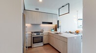 Located along South Indiana Avenue in Chicago's vibrant Near South Side, this single-floor residence showcases a clean, contemporary design with an open, well-connected layout. Light hardwood flooring runs throughout, unifying the living, dining, and kitchen areas into a cohesive and functional space.

The kitchen is outfitted with flat-front light wood cabinetry, under-cabinet lighting, stainless steel appliances including a gas range, and a large peninsula with bar seating — ideal for casual dining or entertaining. Adjacent to the kitchen, the dining area accommodates a full-sized table and benefits from a pendant light fixture overhead, while a built-in wine display adds a refined touch.

The living room is a standout, featuring expansive floor-to-ceiling windows that frame sweeping views of the Chicago skyline, flooding the space with natural light and creating an airy, elevated atmosphere.

The bedroom continues the modern aesthetic with large windows offering additional city views, light wood flooring, and a wall-mounted television. The bathroom features a glass-enclosed walk-in shower with vertically laid white tile, chrome fixtures, and a clean, minimalist vanity — completing the residence's polished, contemporary character.
