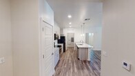 This well-appointed single-floor residence offers a thoughtfully designed layout with contemporary finishes throughout. The open-concept kitchen serves as the heart of the home, showcasing light wood-tone cabinetry, granite-style countertops, and a center island with a built-in sink and pendant lighting overhead. Stainless steel appliances — including a range, microwave, and refrigerator — complete the space, while wood-look flooring extends throughout the main living areas, adding warmth and continuity.

The bedrooms are carpeted for comfort and each features a ceiling fan with light fixture and windows with slatted blinds that allow for natural light control. The primary bedroom includes direct access to a dedicated bathroom and a walk-in closet with built-in shelving. A second bedroom offers similar comfort with its own closet access.

The primary bathroom is equipped with a dual-sink vanity featuring granite-style countertops, light wood cabinetry, a large mirror, and a glass-enclosed walk-in shower. A secondary bathroom provides a single-sink vanity with matching finishes. The dedicated laundry room includes a full-size washer and dryer, open shelving, and houses the electrical panel, offering added practicality. Recessed lighting and a neutral color palette contribute to a clean, modern aesthetic throughout the residence.