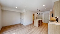 Located on the third floor at 820 N State St in Bellingham, Washington, this thoughtfully designed studio unit offers a compact yet functional single-floor layout. Light wood-tone luxury vinyl plank flooring runs throughout, creating a warm and cohesive aesthetic.

The kitchen is a standout feature, showcasing flat-panel light wood cabinetry extending to the ceiling for ample storage, paired with crisp white quartz countertops. A full suite of stainless steel appliances includes a French door refrigerator, electric range, built-in microwave, and dishwasher. A kitchen island provides additional prep space, and stylish matte black pendant lights overhead add a modern finishing touch.

The open living area benefits from an oversized picture window that floods the room with natural light and offers views of mature trees and the surrounding neighborhood streetscape, providing a pleasant and airy atmosphere.

The bathroom is clean and contemporary, featuring a wood-toned vanity with a stone-finish countertop, a full soaking tub with shower combination, and coordinating matte black fixtures and hardware throughout. White walls and light flooring keep the space feeling bright and fresh.

Overall, the unit presents a modern, minimalist design with consistent finishes and efficient use of space, making it a well-appointed residence in Bellingham's North State Street corridor.