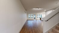 Located on Main Street in the heart of Bellevue, WA, this two-level unit offers a well-designed layout that balances open communal spaces with private retreats. The main level features a spacious living area finished with rich hardwood-style flooring, crisp white walls, and a wall-mounted mini-split system for efficient climate control. Track lighting and recessed fixtures illuminate the space, which opens toward a wall of windows and a glass door that invites natural light and views of the surrounding neighborhood.

The kitchen is a standout feature, showcasing floor-to-ceiling white cabinetry, quartz-style countertops, a subway tile backsplash, and a full suite of stainless steel appliances including a range, microwave, dishwasher, and French door refrigerator. A large central island with pendant lighting above adds both prep space and a casual gathering area.

The lower level includes a secondary living or flex space with hardwood-style flooring, recessed lighting, and direct entry access. Carpeted bedrooms on the upper level offer quiet retreats, with large windows framing exterior views. Closet space is well-provided, including a walk-in with built-in shelving. Bathrooms feature soaking tubs with tile surrounds, wood-look flooring, and clean white vanities with ample storage.