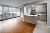 Located at 255 Glenlake Ave in Toronto's desirable High Park neighbourhood, this single-floor unit offers a thoughtfully designed layout with a neutral, contemporary aesthetic throughout. Parquet wood flooring is a consistent and distinctive feature across the living, dining, and bedroom areas, adding warmth and character to the space.

The living area is generously proportioned, benefiting from floor-to-ceiling windows fitted with roller blinds that allow for adjustable natural light while framing elevated views of the surrounding cityscape. A ceiling fan adds a practical touch to this bright, open area. Baseboard heating runs along the perimeter of the windowed walls, ensuring year-round comfort.

The kitchen has been renovated to a modern standard, featuring light wood cabinetry extending to the ceiling, white quartz countertops, and stainless steel appliances including a refrigerator, microwave, and range. A kitchen island provides additional workspace and visual separation from the living area. Light tile flooring completes the clean, functional kitchen design.

The bedrooms maintain the parquet flooring and neutral wall tones found throughout, with windows offering natural light and access to outdoor views. The overall palette of soft greys and warm wood tones creates a calm, cohesive living environment.