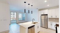 Located at 19 Harnett St in Wilmington, NC, this modern 2-bedroom, 1-bathroom residence offers a thoughtfully designed single-floor layout with clean finishes throughout. The open-concept kitchen and living area serves as the heart of the home, anchored by a central island with quartz countertops, a deep stainless steel single-basin sink, and a matte black faucet. Sleek white cabinetry lines the walls alongside stainless steel appliances, including a refrigerator, microwave, and dishwasher. A tile backsplash and trio of cylindrical pendant lights add a contemporary touch, while light wood-style flooring and access to a private balcony bring warmth and natural light to the space. A carpeted hallway connects the living area to the bedrooms, each finished with soft carpet, ceiling fans, and windows that invite natural light. The primary bedroom includes direct access to a dedicated walk-in closet fitted with wire shelving systems. The bathroom is finished in a crisp, all-white palette, featuring a glass-enclosed walk-in shower, white vanity with quartz countertop, and light wood-style flooring with matte black hardware accents throughout.