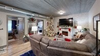 Located in Pigeon Forge, Tennessee, this single-floor space offers a well-designed layout that blends comfort and functionality throughout. The living area serves as the heart of the home, anchored by a white electric fireplace set against a whitewashed brick accent wall. A large wall-mounted television sits above the mantle, while a generous sectional sofa and a round glass-top coffee table create an inviting gathering space. The ceiling features a distinctive industrial-style finish with exposed ductwork, lending the space a modern, urban character complemented by warm hardwood-style flooring.

The kitchen is outfitted with sleek gray cabinetry, granite-style countertops, stainless steel appliances including a French door refrigerator and a range with hood, and a decorative mosaic tile backsplash — delivering both style and practicality for home cooking.

The bedroom provides a restful retreat, highlighted by an ornate wooden headboard, rich navy drapery, and the same whitewashed exposed brick wall that flows throughout the space, adding architectural continuity and charm.

The bathroom is thoughtfully designed with a granite vanity, bold blue tile accent wall, white louvered storage cabinetry, a shower, and a soaking tub, balancing aesthetic appeal with ample storage and functionality.