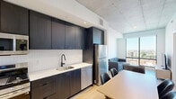 Located at 625 North 2nd Avenue in downtown Phoenix, this modern one-bedroom, one-bathroom unit offers a thoughtfully designed open-concept layout across a single floor. Exposed concrete ceilings throughout lend an industrial-chic aesthetic that complements the clean white walls and light wood flooring found in every room.

The combined kitchen and dining area serves as the heart of the unit. The kitchen features dark, flat-front cabinetry extending to the ceiling, white tile backsplash, white quartz countertops, stainless steel appliances including a gas range, built-in microwave, dishwasher, and refrigerator, and a matte black faucet at the sink. A light wood dining table with seating for four flows naturally from the kitchen space.

The living room opens to a large floor-to-ceiling window, flooding the space with natural light and offering expansive views of the Phoenix skyline and surrounding cityscape. The bedroom continues this view orientation with its own window framing the urban landscape, paired with light wood floors and an exposed concrete ceiling. A dedicated closet provides organized storage. In-unit laundry adds everyday convenience.

The bathroom is finished with large-format wall tile in the walk-in shower with a rain showerhead, grey floor tile, a floating wood vanity, undermount sink, matte black fixtures, and a wide illuminated mirror.