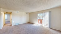 Located at 3821 Village Rd S in Colorado Springs, CO, this single-floor unit offers three bedrooms, one bathroom, and a functional layout across a comfortable footprint. The living area is carpeted and bathed in natural light, with a sliding glass door that opens to a private wood-railed balcony overlooking the tree-lined community and Colorado's open blue skies. Textured ceilings are featured throughout, lending a consistent finish to each room. Two closets provide practical storage solutions, while a connecting hallway links the living spaces efficiently. The generously sized primary bedroom is a standout feature, offering ample space and multiple windows with vertical blinds for adjustable light control. The additional bedrooms are also carpeted, each with their own windows and doors, making them well-suited for a variety of uses. The full bathroom is finished with white subway-style tile surrounding a tub and shower combo, accented by chrome fixtures. A ceiling fan is visible near what appears to be a kitchen area, adding ventilation and comfort. The unit also includes a coat closet at the entry. Overall, the space presents a clean, neutral palette throughout, offering a move-in-ready layout in an established Colorado Springs neighborhood.