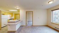 Located at 12740 30th Avenue NE in Seattle's Meadowbrook neighborhood, Unit 333 is a thoughtfully designed single-floor residence with a functional, open-concept layout. The living area is generously proportioned, featuring plush carpeting, neutral walls, and a bright window that invites natural light and views of the surrounding neighborhood. A baseboard heating system runs beneath the window, ensuring year-round comfort.

The kitchen is designed in a galley style, featuring light maple cabinetry, laminate countertops, and wood-look flooring. It is equipped with a full suite of white appliances, including a refrigerator, electric range, and dishwasher, and offers ample cabinet and counter space for storage and meal preparation. A peninsula counter with an overhang seamlessly connects the kitchen to the living area, providing a convenient breakfast bar.

The bedroom is a comfortable, carpeted retreat with a large window overlooking the neighboring building and a sliding-door closet offering generous storage. The bathroom features wood-look flooring, a maple vanity with laminate countertops, and grab bars for added accessibility. Throughout the unit, warm wood-toned trim and door frames provide a cohesive, welcoming aesthetic.