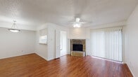 This two-story space is thoughtfully laid out across two distinct levels, each with its own character and function. The main level centers around a welcoming living area finished with rich hardwood-style flooring and a textured ceiling with a ceiling fan overhead. A standout feature is the stone-faced fireplace, accented by a chevron-patterned wood surround that adds a rustic yet stylish focal point to the room. Vertical blinds along a sliding door allow for adjustable natural light. The living area connects seamlessly to the kitchen, which features white cabinetry with detailed panel fronts, light stone-finish countertops, tile flooring, and white appliances including a range and over-the-range microwave. A bathroom on this level offers a wide vanity with ample cabinet storage, a large mirror, tile flooring, and a shower-tub combination. The upper level includes carpeted spaces that provide a quieter, softer environment. An open railing overlooks the stairwell, contributing to an airy feel. Ceiling fans are present throughout both floors, ensuring consistent comfort. The overall ambiance is clean, neutral, and move-in ready.