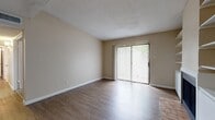 This single-floor residence offers a well-organized layout designed for comfortable everyday living. The main living area is highlighted by wood-look flooring that extends throughout, warm neutral-toned walls, and a textured ceiling. A large sliding glass door fitted with vertical blinds fills the space with natural light and provides direct access to the outdoors, creating an open and airy atmosphere.

Adjacent to the living area, the kitchen is equipped with dark cabinetry contrasting against white countertops, a double sink, a dishwasher, and a full-size refrigerator. Light wood-look flooring continues here, and a pass-through connects seamlessly to the rest of the unit.

The bedrooms are finished with plush carpeting and feature windows with blinds that allow for natural light while maintaining privacy. One bedroom includes a ceiling fan with light fixture, adding both comfort and functionality. A generously sized walk-in closet with built-in shelving and hanging rods provides ample storage.

The bathroom features an extended vanity with a single sink, dark cabinetry below, a wide mirror, and a separate shower-tub combination. Wood-look flooring carries through here as well, maintaining visual consistency across the unit. Overall, the space presents a clean, functional, and cohesive design throughout.