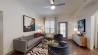This well-designed single-floor residence offers a thoughtfully laid-out interior with a cohesive contemporary aesthetic throughout. The living room serves as the centerpiece of the home, featuring crown molding, hardwood-style flooring, a ceiling fan, and abundant natural light streaming through large windows dressed with white plantation shutters and floor-length drapes. Bold artwork, a chevron-patterned area rug, and a gold-accented glass coffee table lend the space a curated, modern character. A direct-access door opens to an outdoor area, enhancing the connection between interior and exterior. The kitchen is outfitted with white shaker cabinetry, quartz countertops, a tile backsplash, and stainless steel appliances, offering both style and functionality. The dining area accommodates a round wood table with velvet accent chairs beneath a modern chandelier, with colorful framed artwork completing the look. The bedroom is a serene retreat highlighted by a bay window configuration, ceiling fan, crown molding, and warm hardwood-style flooring. The bathroom features an extended white vanity with quartz countertops, dual framed mirrors, and wood-style flooring, delivering a clean, refined finish. Every room reflects a consistent attention to detail and modern elegance.