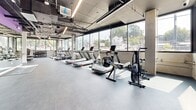 Located at 355 Glendale Blvd in the vibrant Silver Lake neighborhood of Los Angeles, this fitness center offers a comprehensive exercise facility spread across a single, open floor. The space features an industrial-modern aesthetic, with exposed ceiling ductwork and conduit, polished concrete-style flooring, and sleek linear lighting that runs the length of the room.

Large floor-to-ceiling windows line multiple walls, flooding the interior with abundant natural light and offering open views of the surrounding Los Angeles streetscape. The generous open floor plan allows for clear zones dedicated to different types of training.

The cardio area is well-appointed with multiple treadmills, elliptical machines, rowing machines, and stationary bikes, all positioned along the windowed walls to maximize natural light during workouts. The strength and resistance training zone includes a leg press/extension machine and other selectorized equipment. A dedicated functional training area features a wall-mounted storage rack stocked with medicine balls, TRX suspension trainers, and additional accessories. A full dumbbell rack rounds out the free weights section with a wide range of weights available.

The overall ambiance is clean, modern, and energizing, with the combination of bright natural light, open sightlines, and a well-organized layout creating an inviting and fully functional environment for a complete workout.