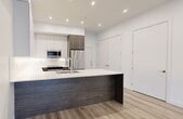 This modern two-bedroom, two-bathroom unit at 10125 114 Street NW, Edmonton, offers a thoughtfully designed single-level layout with a clean, contemporary aesthetic throughout. Light-toned hardwood flooring flows consistently across the living areas and bedrooms, creating a cohesive and bright atmosphere.

The kitchen is a standout feature, showcasing a large island with a dark wood-grain base and quartz countertop, white upper cabinetry, warm wood lower cabinets, and stainless steel appliances including a refrigerator, built-in microwave, and dishwasher. Recessed lighting illuminates the space, reinforcing the modern, open feel.

Both bathrooms are finished with striking marble-style tile on the floors and walls. The main bathroom includes a soaker tub and a wood-accented vanity, while the second bathroom features a glass-enclosed walk-in shower and matching vanity, both exuding a clean, refined look.

The two bedrooms are bright and well-proportioned, each benefiting from windows with roller shades that allow natural light to filter in. The primary bedroom includes a dedicated closet with built-in shelving, providing practical storage. Clean white walls and subtle tray ceiling detailing add architectural interest throughout the unit, resulting in a polished, move-in-ready living space.