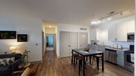 This well-appointed single-floor residence in Huber Heights, Ohio offers a thoughtfully designed open-concept layout that seamlessly connects the kitchen, dining, and living areas. The kitchen is a standout feature, outfitted with stainless steel appliances, granite countertops, two-tone cabinetry in white and gray, a deep undermount sink, and track lighting overhead. A dark-topped kitchen island with bar seating provides an ideal space for casual dining or entertaining. The living room is bright and welcoming, with large French doors topped by transom windows that invite generous natural light and provide outdoor access. Wood-style flooring flows throughout the main living areas, adding warmth and continuity to the space. Two well-sized bedrooms are carpeted for comfort and each features windows that allow ample natural light, creating restful retreats. The unit includes two bathrooms: one with a tub-shower combination and a granite-topped vanity, and another with a walk-in glass-enclosed shower and matching granite vanity. A hallway with a double-door closet offers convenient storage. The overall design balances modern finishes with a neutral, inviting palette that creates a clean and functional living environment.