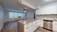 Located at 910 Pennsylvania Ave in Kansas City, MO, this 3-bedroom, 1-bathroom unit offers a practical and modern layout across a single floor. The open-concept kitchen and living area serves as the heart of the home, featuring sleek white cabinetry with brushed nickel hardware, a herringbone tile backsplash, stainless steel appliances including a refrigerator, dishwasher, and range, and a peninsula countertop that provides additional prep and seating space. Warm hardwood-style flooring runs throughout the kitchen and living area, complemented by a ceiling fan that enhances airflow and comfort. The living room receives natural light through a bank of windows fitted with horizontal blinds. The three bedrooms are finished with plush carpeting and each includes a wall-mounted HVAC unit and windows that bring in natural light. The primary bedroom is generously sized and features a sliding-door closet with built-in shelving. The bathroom is cleanly appointed with tile flooring, a wood-toned vanity with open shelving, and a shower-tub combination. A hallway connects the rooms efficiently, completing this well-organized and functional living space.