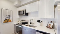 This efficiently designed one-bedroom, one-bathroom unit makes smart use of its single-floor layout, offering a cohesive and modern living experience. The kitchen is a standout feature, showcasing two-tone cabinetry with sleek white upper cabinets and muted gray-blue lower cabinets, all complemented by crisp white countertops and a classic subway tile backsplash. A full suite of stainless steel appliances — including a French door refrigerator, electric range, over-the-range microwave, and dishwasher — provides everything needed for everyday cooking. Light hardwood-style flooring runs throughout, lending warmth and visual continuity to the space. The open layout connects the kitchen to a combined living and dining area, as seen in the dollhouse view, creating an inviting and functional common space. The bedroom, while cozy in scale, is thoughtfully appointed with clean white walls, a flush ceiling light, and double doors that provide privacy and closet access. The bathroom features a full-length vanity with white countertops and warm wood-toned cabinetry, a shower-tub combination, and continued hardwood-style flooring, all set against a bright, white palette. The overall design is clean, modern, and practical — ideal for those seeking a streamlined, move-in-ready living space.