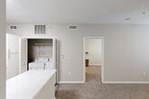 Located at 10770 Barely Lane in Houston, TX, this one-bedroom, one-bathroom unit offers a practical and well-organized single-floor layout. The combined kitchen and living area forms the heart of the space, featuring wood-look tile flooring, crisp white cabinetry, a subway tile backsplash, a light quartz countertop peninsula, and a full suite of stainless steel appliances including a refrigerator, electric range, microwave, and dishwasher. A convenient in-unit laundry area with a full-size washer and dryer is tucked behind louvered doors just off the kitchen, keeping daily tasks easily accessible. A hallway connects the main living area to the private bedroom, which is carpeted and features a ceiling fan with light, a window with blinds that allows natural light, and two dedicated closets for ample storage. The bathroom is clean and functional, offering a tub/shower combination with tiled surround, wood-look flooring, and overhead cabinetry. Neutral gray walls and white trim throughout lend the space a cohesive, move-in-ready aesthetic. The layout is thoughtfully arranged to maximize functionality within a compact and efficient footprint.