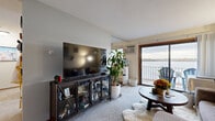 Located at 2479 Commerce Blvd in Mound, Minnesota, this single-floor waterfront unit offers a compelling combination of comfortable living and breathtaking natural surroundings. The living room serves as the heart of the space, featuring carpet flooring, neutral walls, and a sliding glass door that opens onto a private balcony with panoramic views of the adjacent lake. The balcony overlooks a serene wetland shoreline framed by seasonal foliage, providing a tranquil backdrop visible from inside the unit. The kitchen is outfitted with warm oak cabinetry, a smooth-top range, and wood-style flooring, flowing naturally into a dedicated dining area that benefits from the same bright, open feel. Two bedrooms offer comfortable retreats; one includes a ceiling fan and access to natural light through a window with exterior tree views, while the other is carpeted and cozy. Three closets provide practical storage throughout the unit. The full bathroom features a wood-toned vanity, tiled flooring, and a tub-shower combination. A wall-mounted air conditioning unit serves the living area. The overall ambiance is warm and lived-in, with natural light and open water views lending the space a distinctive lakeside character well-suited to the Mound, MN setting.