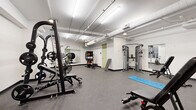 Located at 1965 E Sixth St in Cleveland, Ohio, this fitness center offers a well-appointed, single-floor space designed to support a full range of workout routines. The facility features durable rubber flooring throughout, providing both safety and comfort during exercise. Exposed ductwork and suspended fluorescent lighting run across the white-painted ceiling, lending the space an industrial yet clean aesthetic. Natural light filters in through traditional-style windows along one wall, complementing the bright overhead lighting.

The strength training area is comprehensively equipped with a multi-station cable machine, a Smith machine with an adjustable bench, a set of dumbbells ranging across multiple weights on a tiered rack, and a weight plate storage system. A large wall-mounted mirror enhances the sense of space and allows users to monitor their form during lifts. For cardio and functional training, the facility includes air resistance bikes, a cycling bike, and an interactive training machine. A colorful medicine ball rack adds versatility for functional fitness routines. A SmartMat stretching station provides a dedicated space for warm-up and cool-down. The open floor plan allows for comfortable movement between stations, making this fitness center a practical and well-rounded facility.