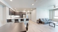 This contemporary residence in San Diego, CA offers a thoughtfully designed single-floor layout with four bedrooms and four bathrooms. The open-concept living, dining, and kitchen area serves as the heart of the home, bathed in recessed lighting and anchored by light-toned hardwood flooring that creates a bright, cohesive aesthetic throughout the common spaces. The modern kitchen is a standout feature, showcasing rich dark cabinetry with sleek hardware, crisp white quartz countertops, a generous island with bar seating, and a full suite of stainless steel appliances including a refrigerator, range, microwave, and dishwasher. The dining area accommodates a full-sized table, while the living room provides a comfortable retreat with neutral-toned walls. Each of the four bedrooms is carpeted for warmth and comfort, with select rooms featuring sliding closets and windows that bring in natural light and open views. The four bathrooms are finished in a clean, minimalist style with white tile surrounds, tub-shower combinations, and wood-toned vanities with white countertops. Recessed lighting throughout the home adds a polished, modern touch, while the neutral color palette ensures a versatile and welcoming atmosphere.