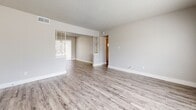 This thoughtfully designed two-bedroom, one-bathroom residence spans a comfortable single floor, offering a clean and modern aesthetic throughout. The open living area features light gray wood-look vinyl flooring, neutral-toned walls, and a textured ceiling that runs consistently across the space. A large window allows natural light to fill the room, creating a bright and welcoming atmosphere. A decorative partition with glass detailing separates the living area from the adjoining space, adding a subtle architectural detail.

The kitchen is well-appointed with white shaker-style cabinetry, granite countertops with warm speckled tones, a stainless steel undermount sink with a modern pull-down faucet, and a stainless steel range. A window above the counter brings in additional natural light, making the kitchen feel open and functional.

Both bedrooms continue the wood-look flooring and neutral palette, each offering a calm and versatile space with natural light from window openings. A hallway connects the bedrooms and bathroom, providing a logical and efficient flow.

The bathroom features matching white cabinetry with granite countertops, a soaking tub, wood-look flooring, and a window for ventilation and light. The consistent design language across all rooms gives this residence a cohesive, move-in-ready feel.