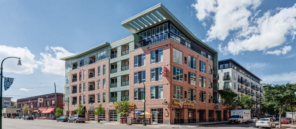 Exterior of a multi-story apartment building with brick and green facade, balconies, and large windows.