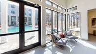 Located in Richmond, VA (23238), this contemporary amenity space is designed to offer residents a high-quality recreational experience across a thoughtfully curated single-floor layout. At the heart of the outdoor area is a large, sparkling resort-style swimming pool surrounded by a generous pool deck lined with lounge chairs and vibrant red umbrellas, providing ample space for relaxation under the open sky. The multi-story building façade, finished in a clean white board-and-batten and brick exterior, frames the pool courtyard with a striking architectural presence. Transitioning indoors, a sunlit lounge area enclosed by floor-to-ceiling windows and glass walls offers sweeping views of the pool deck, filling the space with abundant natural light. Comfortable modern seating invites residents to unwind while staying visually connected to the outdoors. The game room is a standout feature, boasting soaring ceilings and a sophisticated palette of soft blue-gray and white tones. It is equipped with a billiards table, a shuffleboard table, and multiple seating areas with bistro-style tables, making it ideal for social gatherings. Contemporary artwork adorns the walls, adding a curated, gallery-like quality to the space. Together, these amenities create a vibrant, well-designed environment suited for both active recreation and relaxed socializing.
