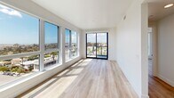 Located at 2525 First Avenue in San Diego's vibrant Hillcrest neighborhood, this modern 2-bedroom, 2-bathroom residence offers a thoughtfully designed open-concept layout bathed in natural light. Light-toned hardwood flooring flows throughout, complementing the clean white walls and contemporary finishes. The combined living, dining, and kitchen area serves as the heart of the home, featuring a striking kitchen with bold navy-blue cabinetry, light upper cabinets, stainless steel appliances, a gas range, and a waterfall-edge marble island with a matte black faucet. Pendant globe lighting and floating wood shelves add stylish, functional touches. Floor-to-ceiling windows in the living area frame breathtaking panoramic views of the San Diego skyline and bay, with a sliding glass door opening to a private balcony. The spacious primary bedroom captures generous city views through a large window bank, while the second bedroom also enjoys an abundance of natural light with its own outdoor outlook. Both bathrooms are finished with crisp white tile, including a soaking tub with subway tile surround and matte black fixtures. Additional conveniences include three closets, a dedicated laundry space, and a hallway connecting all areas seamlessly.