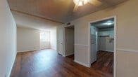 This single-floor residence offers a well-organized layout designed for comfortable everyday living. The main living and dining areas are finished with rich, warm-toned hardwood floors that extend throughout much of the unit, complemented by textured ceilings and a ceiling fan that adds both style and airflow. Exposed ceiling beams add a subtle architectural detail to the main living space, which receives natural light through a window facing the exterior.

The kitchen is equipped with white cabinetry, gray laminate countertops, a double-basin stainless steel sink, a dishwasher, and a white electric range — providing ample storage and functionality. A refrigerator is also included. The kitchen opens conveniently toward the main living area via a half-wall partition.

The two bedrooms are carpeted in a neutral tan tone, each featuring windows with vertical blinds that allow natural light to filter in. The rooms offer clean, open floor space suitable for a variety of furniture arrangements.

The bathroom includes a full-size soaking tub surrounded by classic white subway tile, along with a separate vanity area featuring white cabinetry, a dark laminate countertop, an inset sink, and a lighted mirror above. Hardwood flooring continues into the bathroom, tying the space together cohesively throughout the unit.