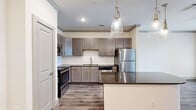 This efficient yet stylish 1-bedroom, 1-bathroom residence is designed to maximize comfort and functionality across a single floor. The open-concept kitchen serves as the heart of the home, featuring warm taupe shaker-style cabinetry, a classic white subway tile backsplash, dark granite countertops, and a full suite of stainless steel appliances including a gas range, built-in microwave, dishwasher, and refrigerator. A curved kitchen island with a dark granite top provides additional prep space and casual seating, while elegant glass pendant lights overhead add a refined touch. Wood-look plank flooring flows throughout the main living areas, lending warmth and cohesion to the space. In-unit washer and dryer hookups offer added convenience. The generously sized bedroom is finished with soft, neutral carpet, a ceiling fan with light fixture, and a window that invites natural light and outdoor views. A dedicated walk-in closet provides ample storage. The bathroom continues the refined aesthetic with dark granite countertops, an undermount sink, and hardwood-style flooring. Crown molding details and recessed lighting throughout elevate the overall ambiance, creating a polished and comfortable living environment.