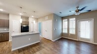 This thoughtfully designed 1-bedroom, 1-bathroom residence offers a comfortable and functional layout across a single floor. The open-concept kitchen and living area serves as the heart of the home, featuring rich hardwood-style flooring, neutral taupe walls, and abundant natural light streaming through multiple windows fitted with white horizontal blinds. The kitchen is well-equipped with granite-style countertops, a large center island with a built-in sink, medium-toned wood cabinetry, black appliances including a refrigerator, electric range, and microwave, along with pendant lighting that adds a modern touch. The living area extends naturally from the kitchen and includes a ceiling fan and access to a private exterior door. The bedroom is a calm, carpeted retreat with dual windows, a ceiling fan, and ample room for furnishings. It connects to a generously sized walk-in closet outfitted with wire shelving and carpeted flooring. The full bathroom features hardwood-style flooring, a tub-shower combination with white tile surround, a vanity with dark cabinetry, and a single sink. Throughout the space, clean white trim and a cohesive neutral palette create a bright, move-in-ready atmosphere.