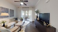 This single-floor residence combines classic architectural details with a clean, contemporary aesthetic throughout its thoughtfully arranged layout. Crown molding and dark hardwood flooring run through the main living areas, lending a polished, cohesive feel. The living room is a comfortable, light-filled space anchored by a ceiling fan, sheer floor-to-ceiling drapes, and sliding glass doors that open onto a private balcony with arched detailing—bringing in generous natural light and outdoor views.

The kitchen features white cabinetry with arched door panels, dark granite-style countertops, and a full suite of appliances, providing ample storage and counter space. A dedicated laundry area houses a full-size washer and dryer with overhead shelving for added utility.

The primary bedroom offers a serene retreat with plush carpeting, large windows dressed in layered window treatments, and direct access to a private bathroom. The en-suite bath includes a vanity with dark countertops, white cabinetry, a well-lit mirror, and a tub-shower combination. A walk-in closet is positioned nearby. The second bedroom is equally well-lit, with generous windows and soft carpeting. Throughout the residence, a neutral color palette and consistent finishes create a calm, inviting atmosphere.