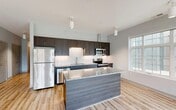 Located at 1420 Merchant Ln in Hampton, VA, this thoughtfully designed two-bedroom, two-bathroom residence offers a comfortable and modern living experience across a single floor. The open-concept kitchen and living area serves as the heart of the home, showcasing dark espresso cabinetry, a classic white subway tile backsplash, granite countertops, and a full suite of stainless steel appliances including a refrigerator, range, microwave, and dishwasher. A central kitchen island with a matching granite surface and wood-toned base provides additional prep space and casual seating. Light hardwood-style flooring flows seamlessly throughout the entire residence, creating a bright and cohesive aesthetic. The living area is bathed in natural light from large, grid-paned windows that offer views of the surrounding neighborhood. Both bedrooms are well-proportioned and quietly appointed, each featuring windows, neutral gray walls, and the same light flooring. The primary bedroom includes a dedicated closet. The two bathrooms are finished with dark wood vanities, granite countertops, and tile flooring that mirrors the warmth found throughout the home. A connecting hallway and two closets complete the efficient and functional floor plan.