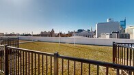 Located at 619 N Broad Street in Philadelphia's vibrant Northern Liberties neighborhood, this rooftop level offers a compelling combination of functional infrastructure and outdoor amenity space. The rooftop is characterized by an expansive green roof system, covered in low-growing vegetation that contributes to energy efficiency and stormwater management. A dedicated terrace area provides an inviting outdoor retreat, furnished with lounge chairs and potted tropical plants set against a backdrop of modern gray horizontal lap siding. Railed walkways and fenced zones partition the rooftop into distinct areas, including mechanical sections housing an array of HVAC units that service the building below. The views from the rooftop are a standout feature, offering unobstructed panoramas of the Philadelphia skyline in multiple directions — capturing Center City landmarks including City Hall and prominent downtown towers to the south, as well as sweeping northward and eastward vistas across the city's diverse architectural fabric. The open-sky setting ensures abundant natural light throughout the day. The rooftop's layout, as revealed by the 3D model, reflects a well-organized design that balances mechanical utility with usable outdoor space, making it a functional and visually engaging level within this urban building.