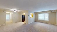 This single-floor residence offers a practical and comfortable layout designed to maximize livability. The spacious living area is anchored by plush wall-to-wall carpeting and a ceiling fan with integrated lighting, creating a bright and airy atmosphere. A large window dressed with horizontal blinds allows natural light to fill the room, while a pass-through opening connects the living area to the kitchen, enhancing the open feel of the space.

The kitchen is equipped with warm oak cabinetry, speckled laminate countertops, and a full suite of black appliances including a gas range, over-the-range microwave, and a full-size refrigerator. A stainless steel sink sits beneath a window, providing natural light during meal preparation. The kitchen features hardwood-style flooring, adding a classic touch.

The bedrooms continue the carpeted aesthetic and each include ceiling fans and windows with blinds that invite natural light. Closet doors are present in the bedrooms, offering ample storage. The bathroom is clean and functional, featuring a single-sink vanity with wood cabinetry and speckled countertop, a full tub-shower combination, and hardwood-style flooring. Overall, the space presents a cohesive, neutral palette throughout.