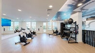 Located at 11401 Biography Way in Orlando, FL, this fitness center offers a thoughtfully designed workout space across a single floor. The main exercise area features light hardwood-style flooring that gives the space a clean, modern feel. Large windows lining the walls flood the room with abundant natural light and provide views of the surrounding outdoor landscape, including palm trees and a pool area.

The space is equipped with a variety of Matrix-brand cardio machines, including multiple stationary spin bikes and a rowing machine, arranged to maximize floor space. A dedicated strength and functional training zone features a multi-tier equipment rack stocked with stability balls, foam rollers, and resistance accessories, alongside a BOSU balance trainer.

Full-length wall mirrors visually expand the space and are complemented by a large mounted flat-screen display, ideal for guided workouts. A standout design element is the dramatic artistic ceiling mural, depicting a celestial sky, which adds a distinctive visual character to the room. A large black-and-white Florida-themed mural further enhances the walls, giving the fitness center a unique, immersive ambiance.

The space also includes a balcony, accessible via glass-paneled doors, extending the functional area outdoors. Recessed lighting throughout ensures consistent illumination, making this fitness center both practical and visually dynamic.