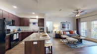 Located at 130 Town Center Blvd in Clermont, FL, this 2-bedroom, 2-bathroom single-floor residence offers a well-designed open-concept layout that seamlessly connects the kitchen, dining, and living areas. The kitchen is a standout feature, showcasing rich dark-wood cabinetry reaching to the ceiling, granite countertops, black appliances, and a center island with bar seating — ideal for both everyday meals and entertaining. Wood-style flooring flows throughout the main living areas, adding warmth and continuity to the space. The living room is bright and inviting, with a ceiling fan overhead and French doors that bring in natural light and provide access to an outdoor area. The primary bedroom is generously sized with plush carpeting, a ceiling fan, and direct access to its own bathroom. Both bedrooms are served by well-appointed bathrooms, one featuring a soaking tub and shower combination with granite vanity accents. Two closets, including a walk-in with wire shelving, provide ample storage. A dedicated laundry room houses a full-size washer and dryer. A hallway with track lighting connects the private quarters to the shared living spaces, creating a functional and cohesive flow throughout the home.