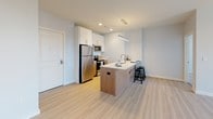 Located at 200 Pleasant St in Malden, MA, this single-floor residence presents a clean, contemporary design throughout. The open-concept living and kitchen area serves as the heart of the unit, featuring light wood-tone flooring that enhances the bright, airy atmosphere. The kitchen is well-appointed with stainless steel appliances, including a refrigerator, microwave, and range, complemented by white upper cabinetry and warm wood-toned lower cabinetry. A peninsula with a light stone countertop and bar seating provides both additional workspace and a casual dining option, illuminated by a sleek linear pendant light overhead.

The two bedrooms offer a comfortable retreat, each finished with plush neutral carpeting and windows that invite natural light and urban views of the surrounding Malden streetscape. The primary bathroom features a glass-enclosed walk-in shower, a floating wood-toned vanity with a white countertop, and large-format tile flooring. The second bathroom includes a tiled tub-shower combination, a matching floating vanity, and a wide mirror with overhead lighting. Neutral tones and recessed lighting throughout the unit contribute to a cohesive, modern aesthetic.