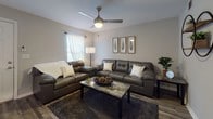 This single-floor residence offers a cohesive layout designed for comfortable everyday living. The kitchen is well-equipped with warm-toned wood cabinetry extending to the upper walls, light granite-style countertops, and a full suite of stainless steel appliances including a refrigerator, electric range, and over-the-range microwave. A double stainless steel sink sits beneath a window that brings in natural light, complementing the durable wood-look flooring found throughout the unit.

The living area provides a generous, open feel with neutral gray walls, wood-look flooring, and a ceiling fan with integrated lighting. Natural light filters in through windows dressed with sheer curtains, creating a bright and relaxed atmosphere.

The bedroom features the same wood-look flooring and neutral tones, with a ceiling fan, natural light from a window with blinds, and ample space for a desk and furnishings. An additional room with a ceiling fan offers flexible use as a second bedroom or office.

Both bathrooms share a consistent design language, each featuring granite-style countertops, warm wood vanity cabinetry, a large mirror, and a tub-shower combination. The overall aesthetic throughout the unit is clean, functional, and cohesive.