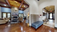 This single-story community clubhouse offers a thoughtfully designed set of amenities suited for both relaxation and productivity. The centerpiece of the space is a grand lounge area distinguished by soaring ceilings with rich, dark wood beam detailing and a striking floor-to-ceiling stacked stone fireplace with a wood mantel. Warm hardwood floors, a statement chandelier, and French doors that invite natural light from the outdoors contribute to the inviting, upscale ambiance. Adjacent to the lounge is a business center equipped with built-in wooden cabinetry, granite countertops, a workstation, and printing capabilities — ideal for those who need a quiet, productive environment. A fully functional kitchen features stainless steel appliances, rich wood cabinetry, granite countertops, and tile flooring, providing a convenient space for hosting or everyday use. The fitness center is well-equipped with treadmills, stationary bikes, medicine balls, and wall-to-wall mirrors, with large windows offering views of the surrounding landscape. A dedicated laundry room rounds out the amenities, offering multiple washer and dryer units for shared use. Throughout, the space maintains a cohesive design with warm tones, quality finishes, and purposeful layouts.