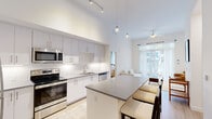 Located at 1710 N Congress Ave in West Palm Beach, FL, this modern single-floor residence offers four bedrooms and two well-appointed bathrooms. The open-concept layout seamlessly connects the kitchen, dining, and living areas, creating a bright and functional living space. The kitchen is a standout feature, boasting soaring ceilings, sleek white cabinetry, a subway tile backsplash, stainless steel appliances, and a large central island with a gray quartz countertop that provides ample seating. Pendant lighting and track lighting complement the airy, high-ceiling design. The living room is bathed in natural light from floor-to-ceiling sliding glass doors framed by sheer white curtains, offering outdoor views and access to a patio area. The dining area accommodates a round glass-top table, adding a clean, contemporary touch. The generously sized primary bedroom features large windows with outdoor views and a dedicated walk-in closet with built-in shelving. Both bathrooms are finished with large-format tile, wide-mirror vanities featuring gray quartz countertops, white cabinetry, and glass-enclosed showers. Light wood-tone flooring runs throughout, enhancing the clean, modern aesthetic of the entire residence.