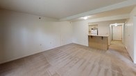 This single-floor residence offers a practical and comfortable layout designed for everyday living. The main living area is generously sized, featuring neutral-toned carpet, a textured ceiling, and a combination of a window and glass door that invite natural light and provide views of the surrounding greenery outdoors. An open pass-through connects the living space to the kitchen, which includes wood-toned cabinetry, a countertop bar overhang ideal for casual dining, and a refrigerator, creating a functional and accessible cooking environment.

The bedroom is well-proportioned with soft carpeting, a large window offering pleasant outdoor views, and direct access to a spacious walk-in closet. The walk-in closet is outfitted with a wire shelving system, including wall-mounted shelving rods and a freestanding multi-tier basket unit, providing ample and organized storage capacity.

The full bathroom features warm earth-toned tile flooring, a standard tub and shower combination, a single-sink vanity with under-sink cabinetry, and chrome fixtures. A dedicated laundry room houses a full-size washer and dryer, accompanied by an overhead wire shelf for added storage convenience. Throughout the unit, a neutral color palette and consistent flooring create a cohesive and move-in ready atmosphere.