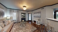 This well-designed single-floor residence offers a cohesive modern aesthetic throughout, characterized by rich dark hardwood-style flooring, dark crown molding, and a neutral color palette that creates a warm, sophisticated ambiance.

The living room serves as the heart of the space, featuring an electric fireplace set within a sleek white media console, large windows dressed with elegant draping curtains that invite natural light, and a decorative ceiling fixture. Large-scale artwork adorns the walls, complementing the refined atmosphere.

The kitchen is a standout, outfitted with grey cabinetry, white quartz-style countertops, a mosaic tile backsplash, and a full suite of stainless steel appliances including a refrigerator, electric range, over-the-range microwave, and dishwasher. The layout is efficient and functional, with ample cabinet storage and counter workspace.

The bedroom is a comfortable retreat, highlighted by a ceiling fan, natural light from a curtained window, dark crown molding, and access to a closet with louvered doors. The room offers a calm and restful environment.

The bathroom includes a tub and shower combination with a curtain enclosure, dark cabinetry with contemporary hardware, and coordinating countertops, maintaining the modern design language found throughout the residence.