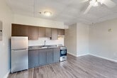 Located in Worcester, MA, this one-bedroom, one-bathroom unit offers a practical and efficiently designed single-floor layout. The open-concept living, dining, and kitchen area forms the heart of the space, featuring light gray hardwood-style flooring that runs throughout and neutral gray walls that create a clean, cohesive aesthetic. Ceiling fans are present in both the main living area and bedroom, contributing to comfort year-round. Multiple double-hung windows flood the living and bedroom areas with natural light while offering views of the surrounding urban streetscape. Baseboard heating units are positioned throughout, ensuring consistent warmth. The kitchen is equipped with gray lower cabinetry, taupe upper cabinets, a stainless steel sink, a refrigerator, and a freestanding range with oven. A suspended tile ceiling defines the kitchen zone, transitioning into the open living and dining area. A hallway connects the main living space to the private bedroom, which benefits from its own window and baseboard heating, as well as a dedicated closet. The bathroom features warm-toned tile flooring and includes built-in shelving along one wall. Throughout the unit, white panel doors and clean white trim provide a crisp finishing touch to this straightforward and functional urban residence.