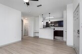 This single-floor residence in Huntsville, Alabama offers a clean, modern layout designed for comfortable everyday living. The open-concept main living area is finished with light wood-style flooring that extends throughout, creating a bright and cohesive feel. A ceiling fan overhead and a glass-panel exterior door allow natural light to fill the space, while a built-in desk nook adds a thoughtful functional touch.

The kitchen is positioned adjacent to the living area and features a peninsula with pendant lighting, rich dark wood cabinetry, light countertops, and a full suite of stainless steel appliances including a refrigerator, microwave, and range. Tile flooring grounds the kitchen space, complementing the warm cabinetry tones.

The bedroom is carpeted for comfort and includes a ceiling fan, a window with blinds for natural light and privacy, and access to additional rooms. The bathroom is finished with tile flooring and includes a single-sink vanity with dark wood cabinetry, a lighted mirror, a full soaking tub with shower, and safety grab bars. The overall palette throughout the unit is neutral and inviting, with white walls and clean finishes that offer a move-in-ready canvas.