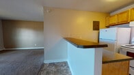 Located at 1039 S Parker Rd in Denver, Colorado, this single-floor unit offers a practical and functional layout designed for comfortable everyday living. The open-concept living area features wall-to-wall carpet, neutral-toned walls, and a textured ceiling, creating a clean and understated atmosphere throughout. A sliding glass door fills the living space with natural light and provides direct access to a private balcony, offering pleasant outdoor views of the surrounding neighborhood. A wall-mounted air conditioning unit and baseboard heating ensure year-round climate control.

The kitchen is efficiently laid out and separated from the living area by a peninsula counter with a dark laminate top, providing additional prep space and a casual dining option. Warm wood-toned cabinetry lines the upper and lower sections of the kitchen, complemented by a white electric range, refrigerator, and a double-basin sink. Tile flooring in the kitchen adds a practical contrast to the carpeted living spaces.

The bathroom includes a full-sized tub and shower combination with clean white tile surround, a toilet, and built-in storage. The unit's straightforward single-floor design ensures easy navigation, making it a well-suited space for those seeking a low-maintenance residence in the Denver area.