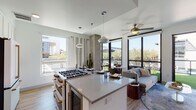 This single-floor residence showcases a contemporary design aesthetic defined by clean lines, light-toned finishes, and an abundance of natural light throughout. The open-concept living and kitchen area serves as the heart of the home, where large black-framed floor-to-ceiling windows and a glass door frame sweeping views of palm trees and a lush outdoor green space, which is directly accessible from the living room. Ceiling fans and pendant lighting complement the bright, airy atmosphere.

The kitchen is outfitted with white shaker cabinetry, a chevron-patterned tile backsplash, quartz countertops, and a spacious center island with seating. Premium appliances include a professional-grade gas range, a French door refrigerator, and a built-in microwave, all accented with rose gold hardware.

Two well-appointed bedrooms offer a calm retreat, each featuring wood-look flooring, ceiling fans, and generous windows with outdoor views. The two bathrooms are finished with large-format gray tile, white vanities with quartz counters, and gold fixtures throughout. One bathroom features a walk-in glass shower with a rain showerhead, while the other includes a soaking tub-shower combination. Wood-look flooring flows consistently throughout the entire residence.