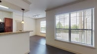This single-story, one-bedroom, one-bathroom unit offers a thoughtfully designed open-concept layout that seamlessly connects the kitchen, dining, and living areas. Dark hardwood-style flooring runs throughout the main living spaces, creating a warm, cohesive aesthetic complemented by neutral wall tones and white trim. Multiple large windows fitted with horizontal blinds flood the interior with natural light and offer views of surrounding greenery.

The kitchen is anchored by rich mahogany-toned cabinetry, granite-style countertops, and black appliances including a range and overhead microwave. A peninsula with pendant lighting serves as both a prep space and casual dining area, while a ceiling fan with a light fixture overhead enhances airflow throughout the open living zone.

The bedroom is generously proportioned, featuring a ceiling fan, dark hardwood-style flooring, and a walk-in closet with built-in shelving, providing ample storage. Additional windows bring in natural light and outdoor views, adding to the room's airy feel.

The bathroom is well-equipped with a dual-sink vanity featuring dark wood cabinetry and granite-style countertops, an expansive mirror, and a full tub-shower combination finished with neutral tile surround. Light tile flooring completes the clean, functional design of this space.