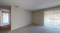 This single-floor residence offers a practical and comfortable layout designed with everyday living in mind. The living area is spacious and open, featuring soft wall-to-wall carpeting in a neutral tone and a textured ceiling throughout. A sliding glass door with vertical blinds fills the room with natural light and provides outdoor access, while the front entry door — accented with glass panel inserts — adds a welcoming touch.

The bedroom areas share the same carpeted flooring and neutral wall tones, each equipped with large windows dressed in vertical blinds that allow for abundant natural light and outdoor views. The rooms provide generous wall space and multiple electrical outlets, offering flexible furniture arrangement.

The kitchen transitions to wood-look plank flooring and features dark cabinetry with brushed nickel hardware, white countertops, and a full-size black refrigerator. Ample counter space and cabinetry on both sides of the galley-style kitchen make it functional and efficient. A doorway from the kitchen connects seamlessly to the main living space.

The bathroom is finished with wood-look flooring and includes a full tub-and-shower combination with white tile surround and chrome fixtures. The overall design of this unit is clean, cohesive, and move-in ready.