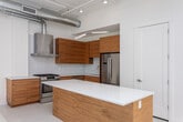 Located in the heart of downtown Salt Lake City, this modern loft-style residence blends industrial character with contemporary finishes across a generously sized single-floor layout. Soaring ceilings with exposed ductwork, structural beams, and track lighting define the industrial aesthetic throughout, while light hardwood flooring and an all-white palette keep the space bright and airy.

The open-concept living area is a standout, featuring expansive floor-to-ceiling glass doors that flood the room with natural light and frame sweeping city views. A ceiling fan adds a functional touch to this impressive main space. The kitchen is well-appointed with rich warm-toned wood cabinetry, white quartz countertops, stainless steel Bosch appliances including a gas range, a stainless hood vent, and a large central island — ideal for cooking and entertaining.

The bedroom offers a comfortable, carpeted retreat with a double-door closet and exposed ceiling details consistent with the loft's industrial style. Three thoughtfully designed bathrooms serve the residence — one features a floating wood vanity with a white countertop and a glass-enclosed walk-in shower, while the primary bath includes both a soaking tub and a separate walk-in shower, with large-format white tile and warm wood cabinetry. Concrete accent walls add raw texture to the space's refined design.