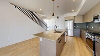 Located in Millcreek, Utah, this contemporary multi-floor residence offers a thoughtfully designed layout spread across three levels. The main floor features an open-concept kitchen and living area anchored by a large center island with quartz countertops, an undermount sink, and sleek pendant lighting. Light wood flooring, recessed lighting, and a bold horizontal-rail staircase add modern character to the shared living space. Stainless steel appliances and two-tone cabinetry complete the well-appointed kitchen. The upper floor houses two generously sized bedrooms, including a spacious primary suite with a walk-in closet featuring built-in shelving and hanging rods. Large windows throughout bring in abundant natural light and frame views of the surrounding Millcreek neighborhood and distant mountains. The four bathrooms are finished in a clean, minimalist style with wood-look flooring and matte black fixtures. A striking open-riser staircase with dark steel railings connects all three levels. The top floor opens onto a private rooftop terrace with panoramic views of the Salt Lake Valley and the Wasatch mountain range — an exceptional outdoor retreat ideal for relaxing or entertaining.